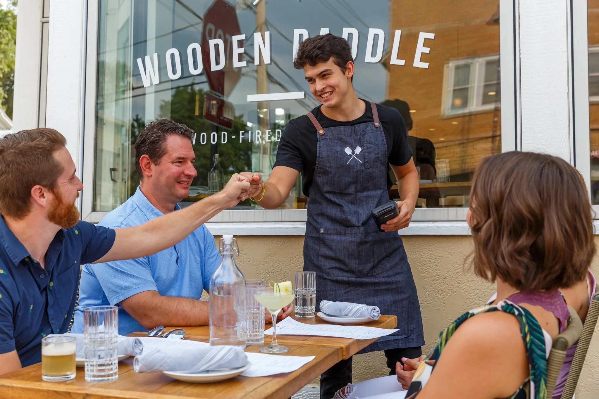 A photo of four restaurant patrons and a staff member enjoying a meal on the patio at Wooden Paddle in Lemont, Illinois.