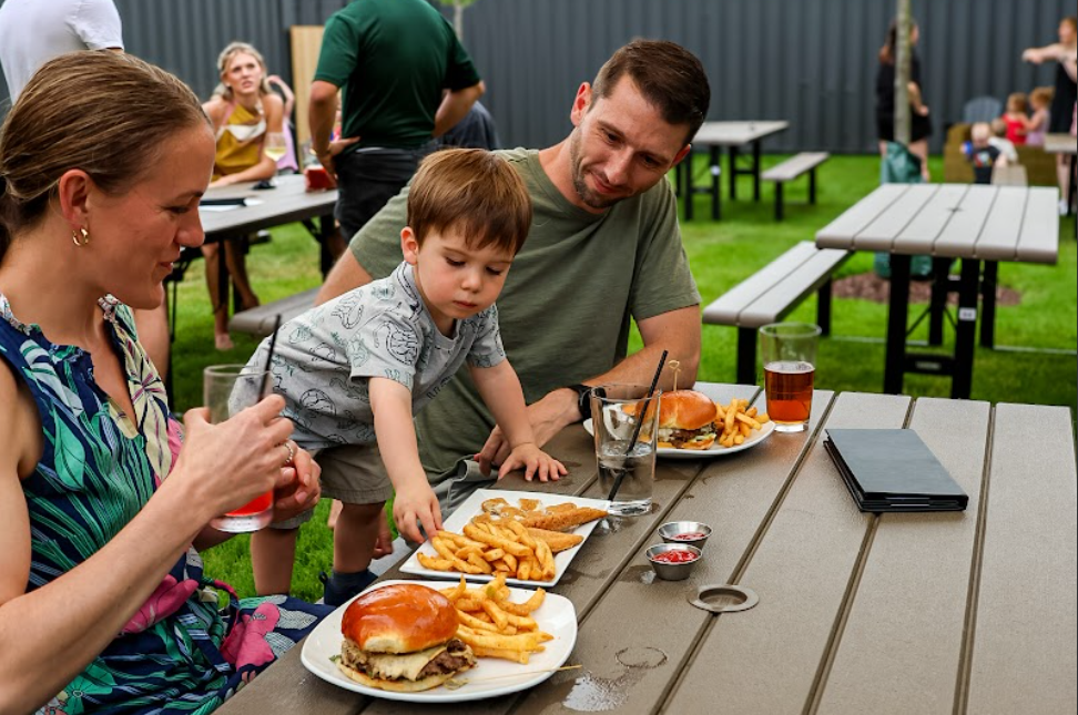 A photo of a mother, father, and son enjoying an outdoor meal on the patio at The Club, a restaurant in Lemont Downtown.