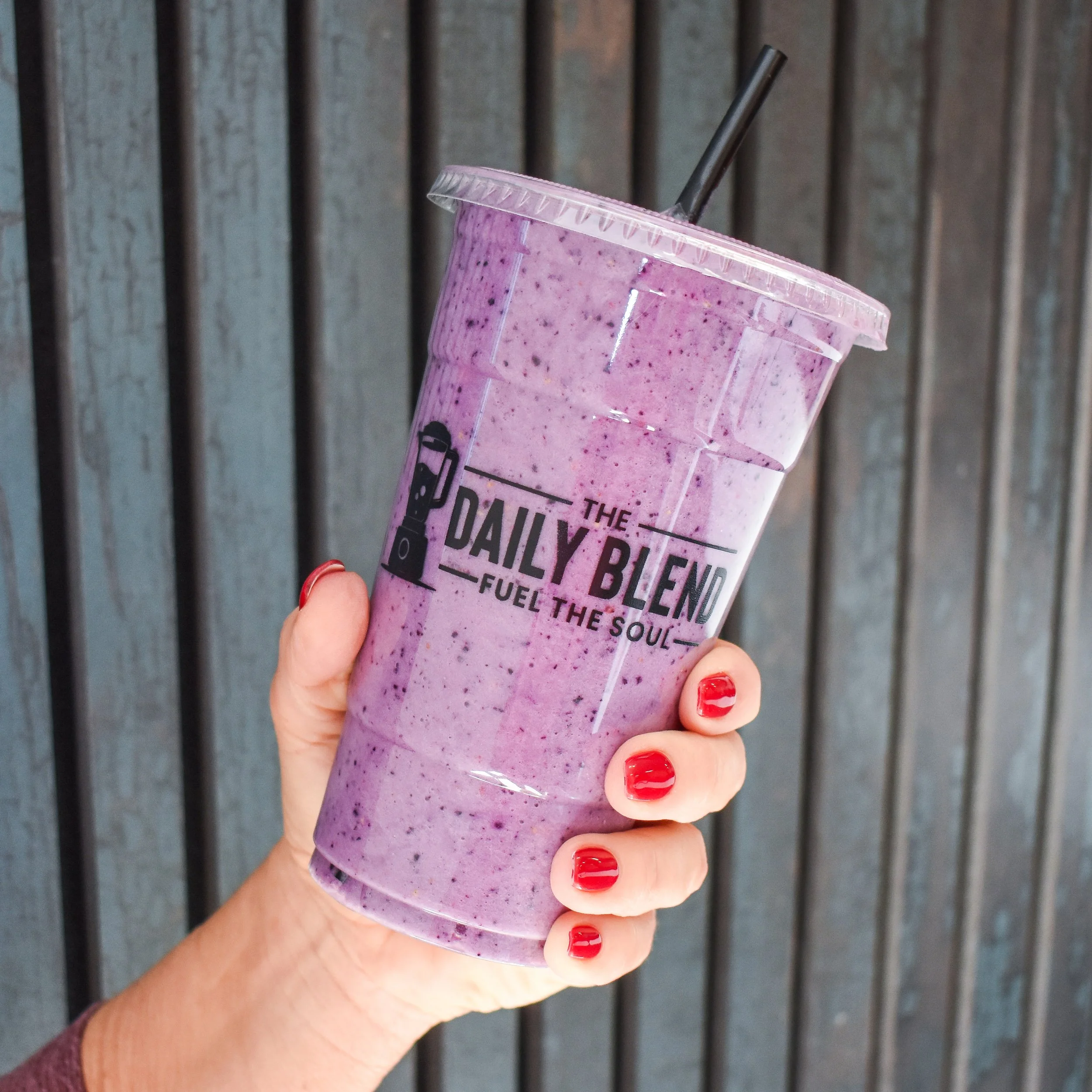 A hand with red nail polish holding a berry smoothie from The Daily Blend