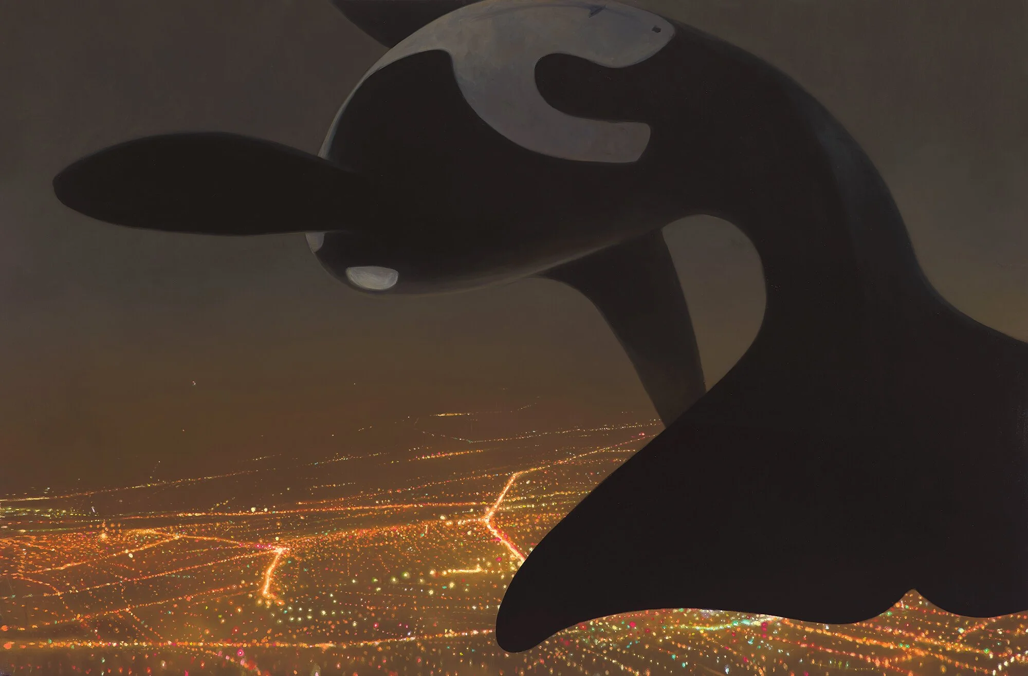 A close-up of a large black and white orca whale figure suspended in the air at night with a cityscape illuminated by lights in the background.