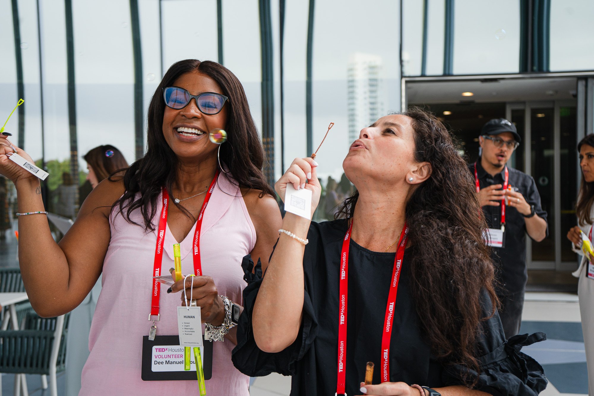 Two women at TedxHouston blowing bubbles. Candid event photography.