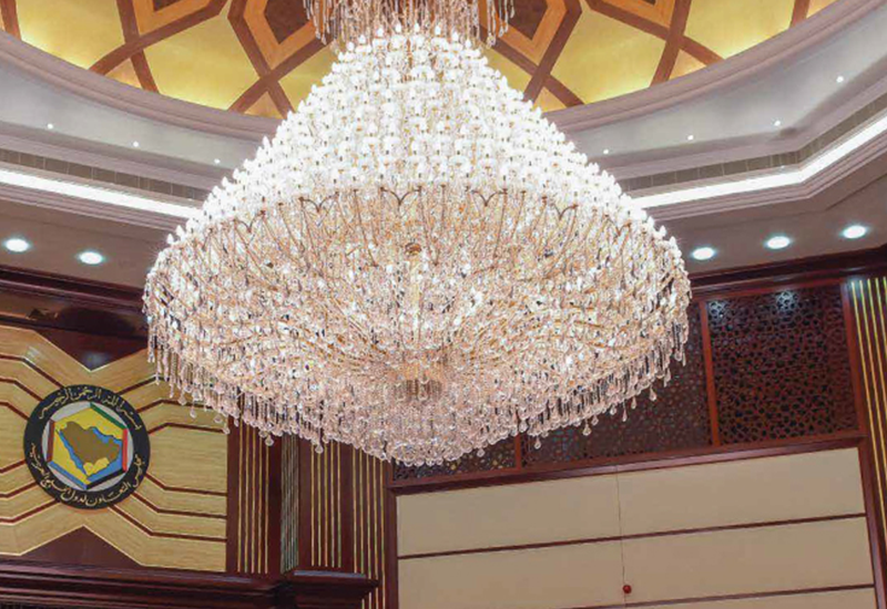 Large crystal chandelier hanging from a decorative ceiling in an elegant room with wood paneling.