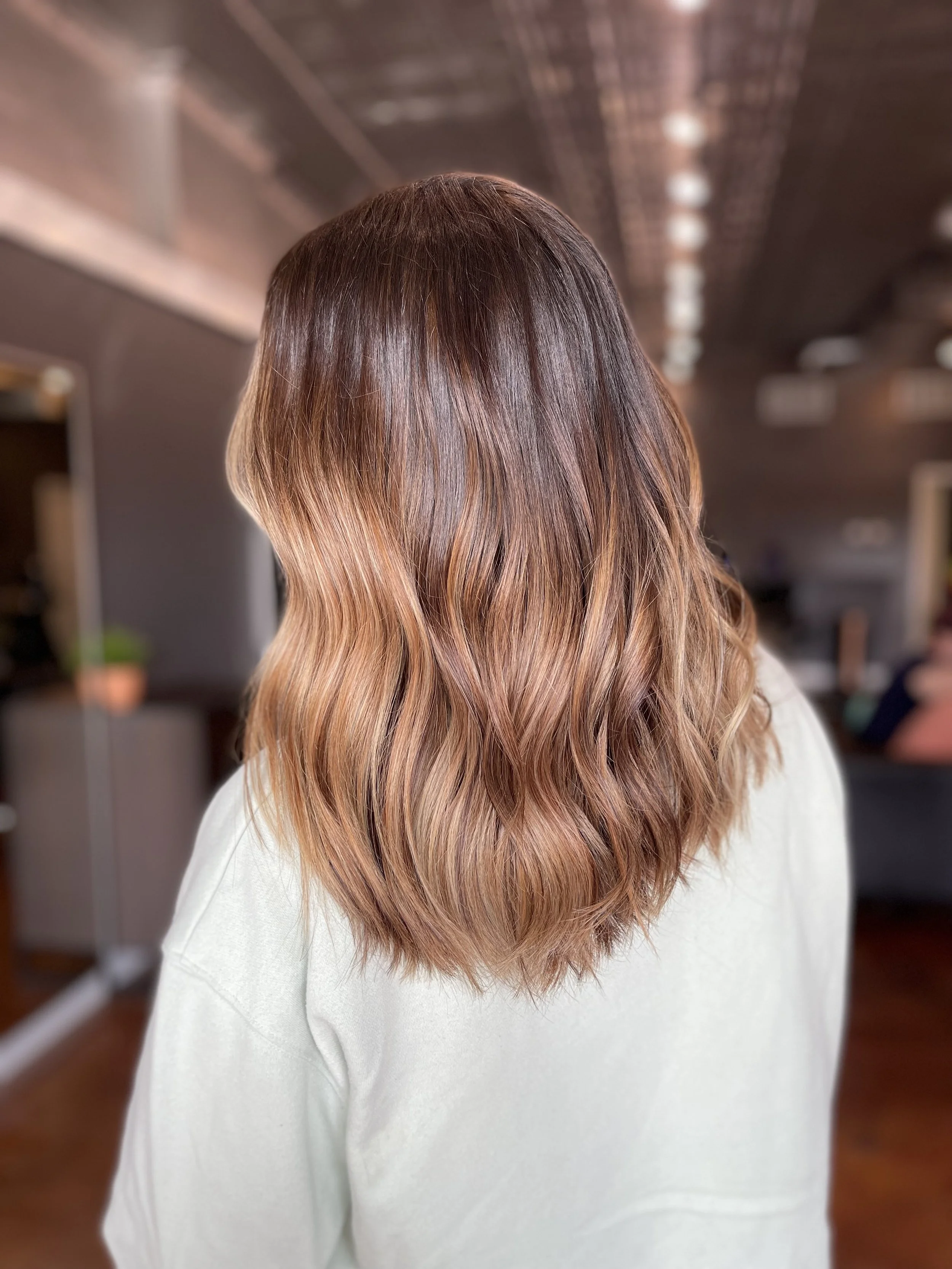 Soft caramel balayage with waves on medium-length hair, styled at The Nicole Martin Salon in St. Louis.