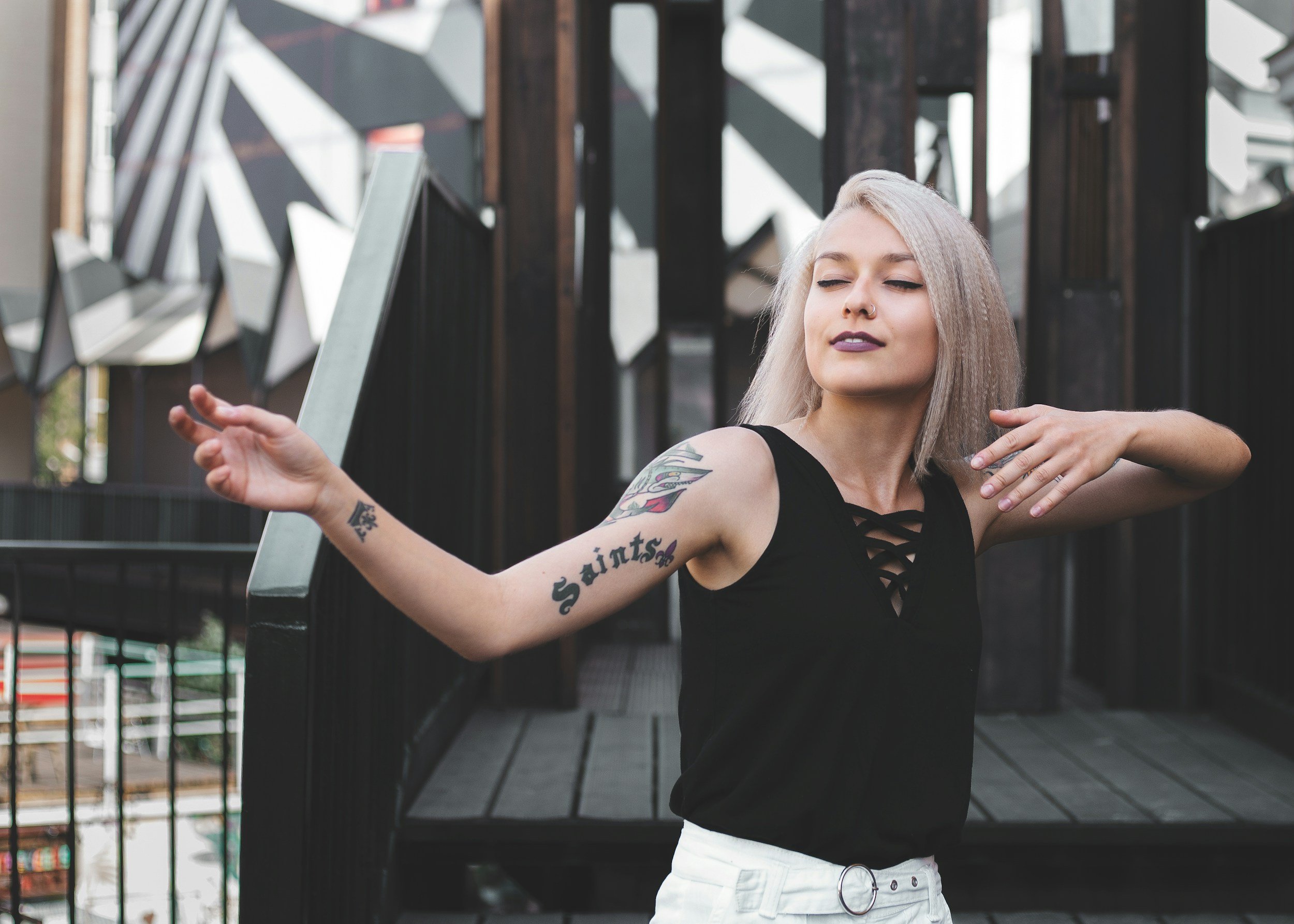 Woman with shoulder-length silver hair and purple lipstick with three tattoos on her right arm it's closing her eyes and shining into her body.