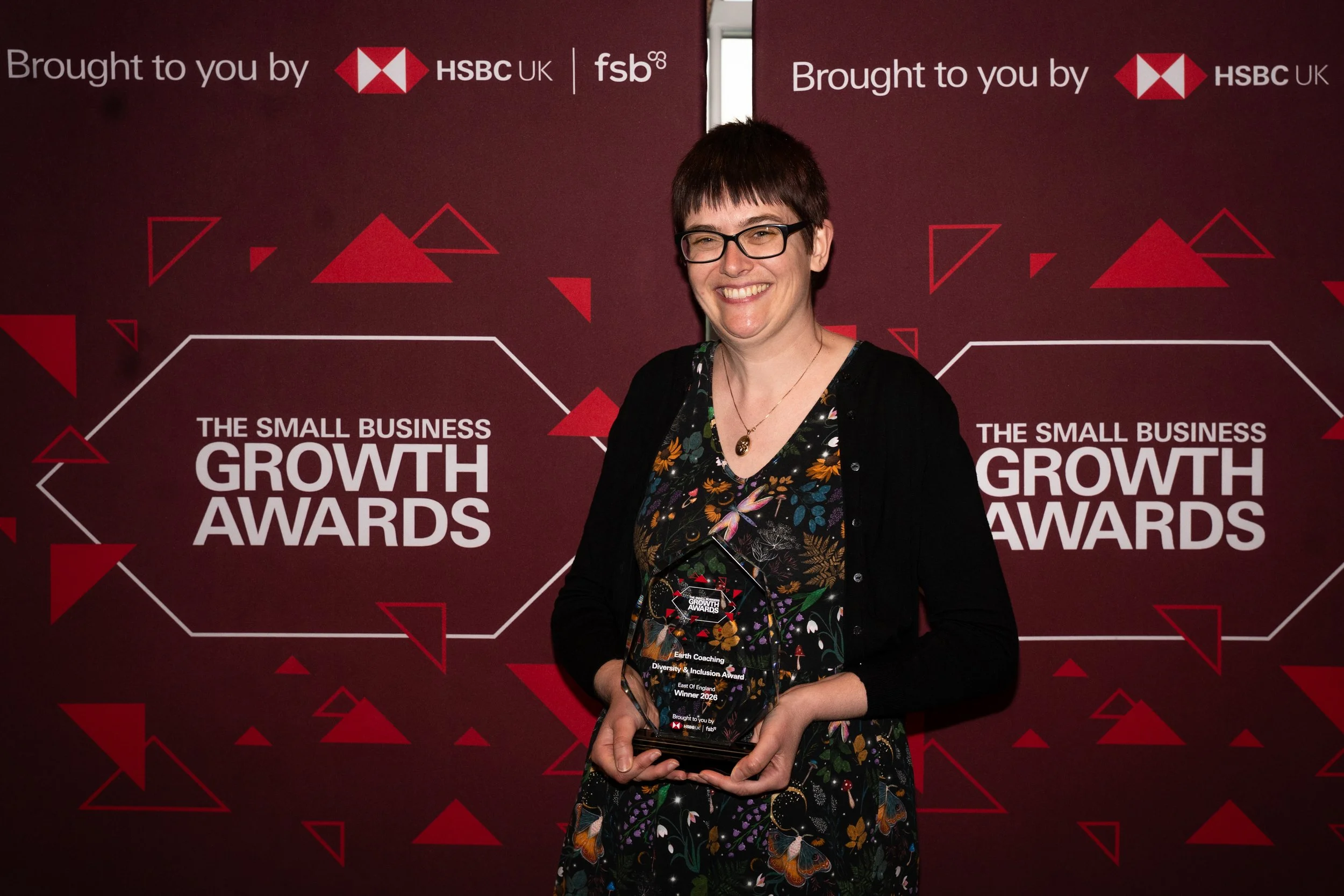 Bex holds an award that says Earth Coaching FSB East of England Diversion & Inclusion Winner 2026 against a red backgroup with HSBC and FSB logos