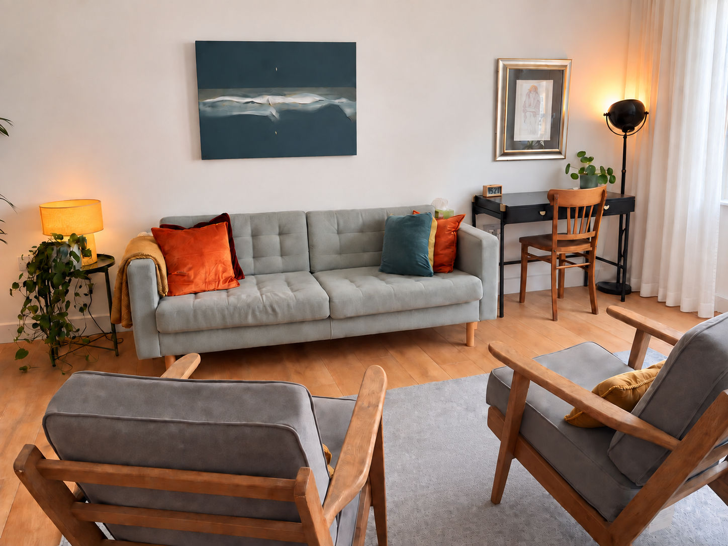 Therapy room with a grey sofa, two wooden armchairs, plants and warm lighting.