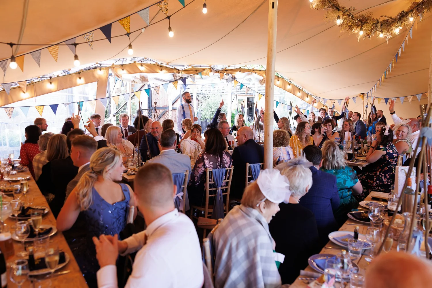 Guests at the wedding breakfast under festoon lights, Jenners Barn