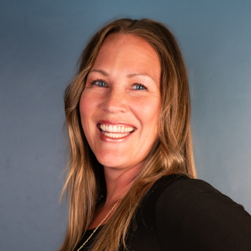 A woman with long blonde hair smiling against a blue background.