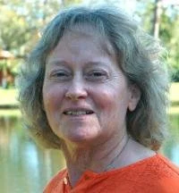 A woman with curly gray hair smiling outdoors near a body of water