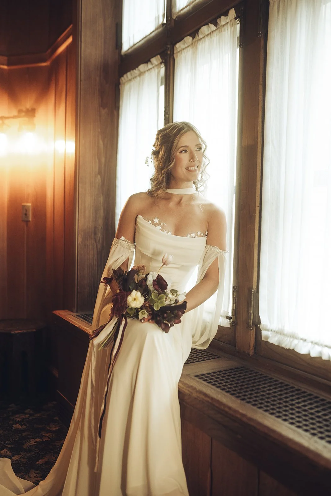 Outdoor wooden arch decorated with white roses, pampas grass, and greenery, against a natural backdrop.