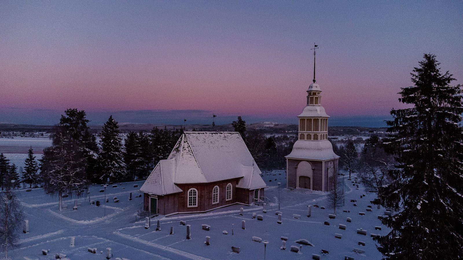 träkyrka i svenska lappland belägen i ett vinterlandskap med blå och rosa himmel.