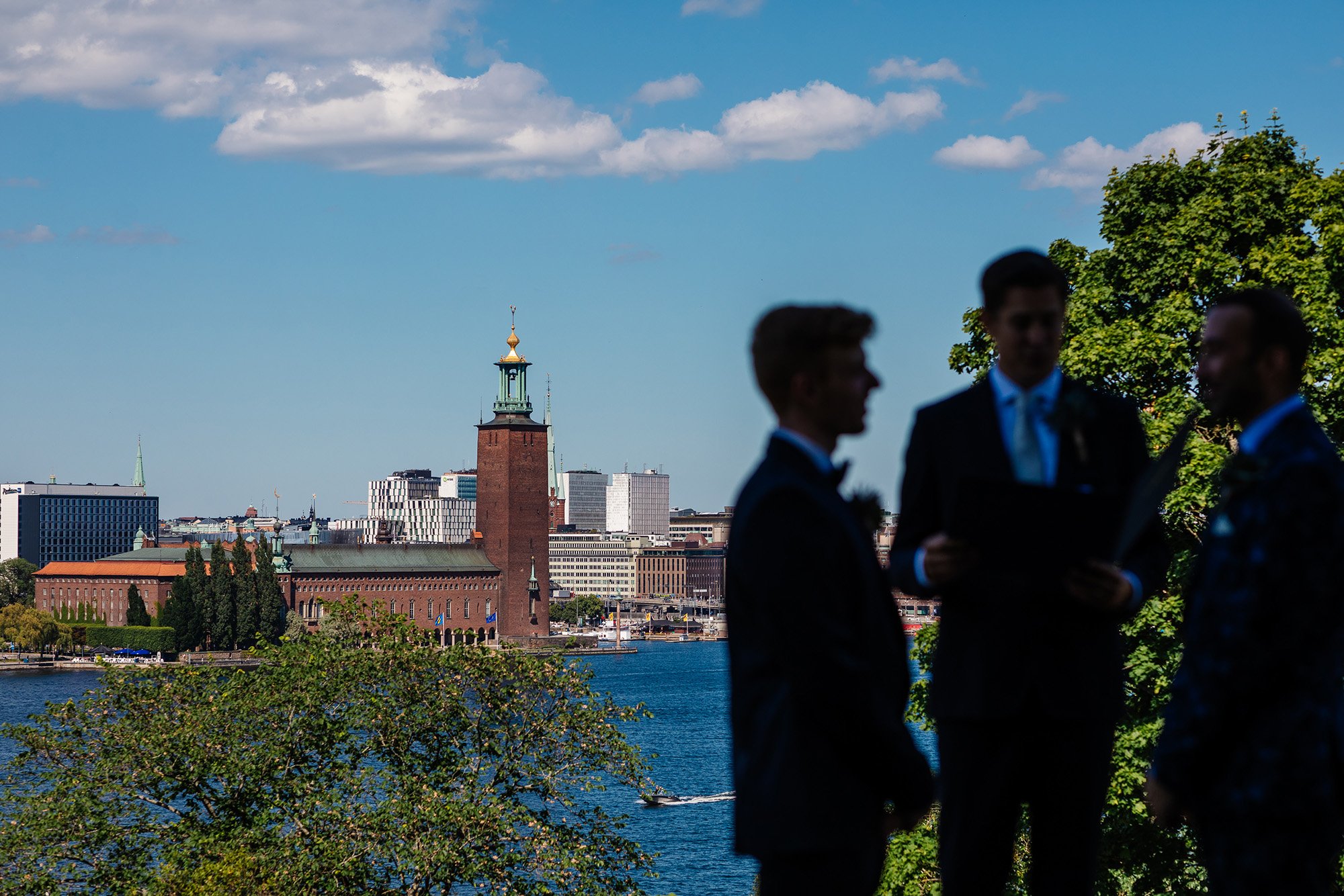 Stockholms stadshus i bakgrunden av siluetter av tre män som genomför en borgerlig ceremoni.