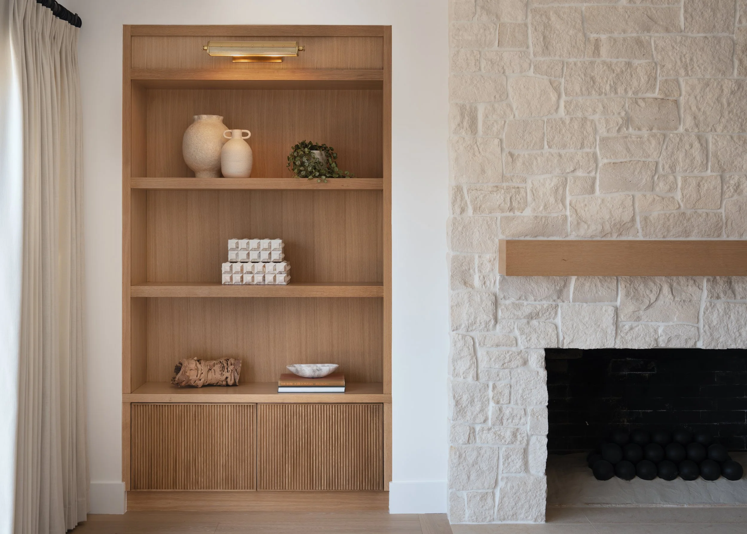 Custom built-in shelving in white oak and stone fireplace remodel in Newport Beach, CA