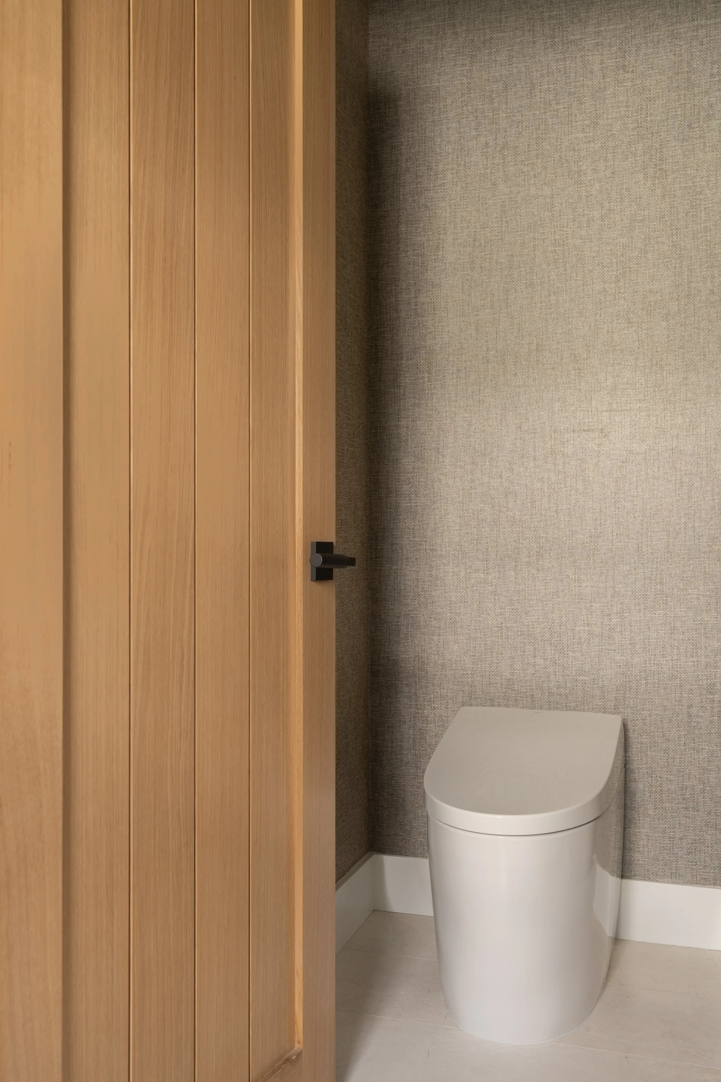 Water closet with wallpaper and white oak door