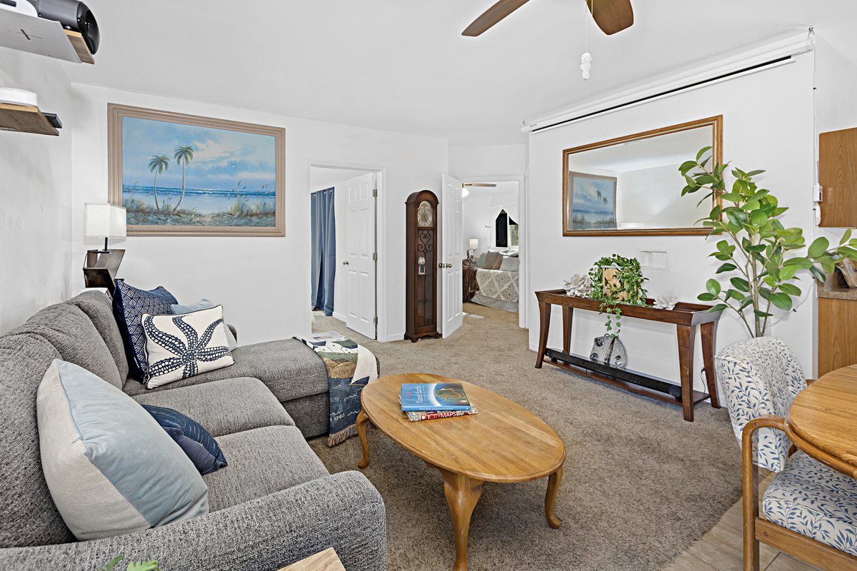 Living room with a gray sofa, wooden coffee table with magazines, large mirror on the wall, potted plant, and doorways leading to other rooms.