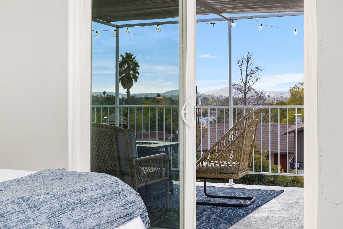 View of a balcony with two chairs, string lights, and a scenic landscape including trees and mountains in the distance.