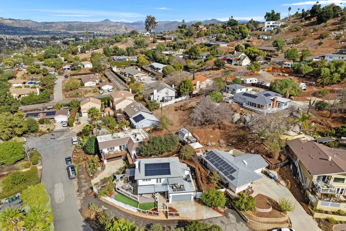 Aerial view of a suburban neighborhood with houses, trees, and hills in the background.