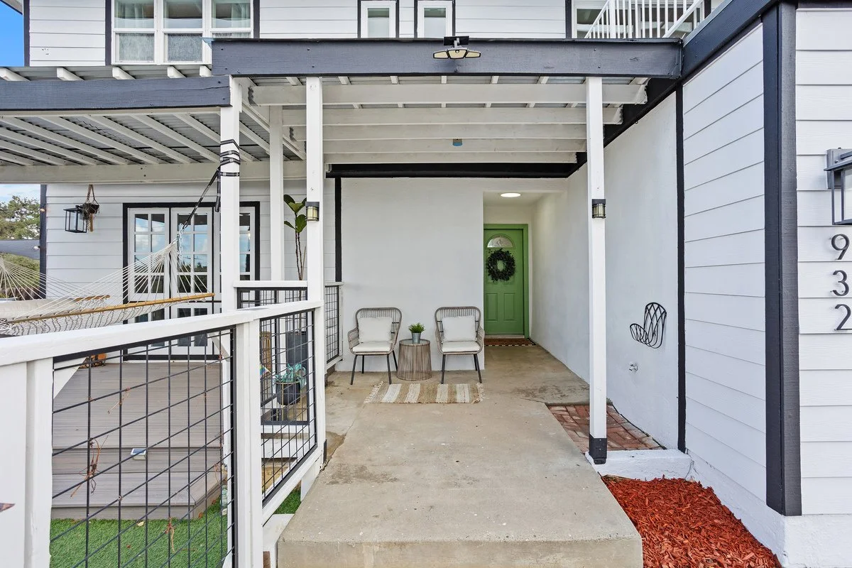 Front porch with two chairs, a small side table, and a green front door adorned with a wreath.