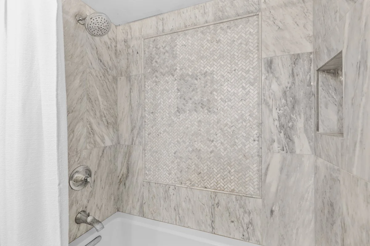 Close-up of a marble shower wall with a built-in niche and a patterned tile accent area.