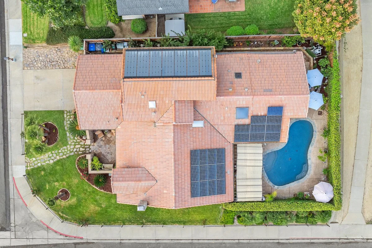 Aerial view of a house with a backyard pool, solar panels on the roof, and a garden with trees and shrubs.