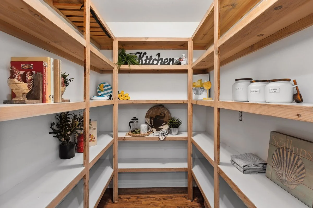 Empty wooden kitchen shelves with decorative items, books, plants, and kitchenware organized on them.