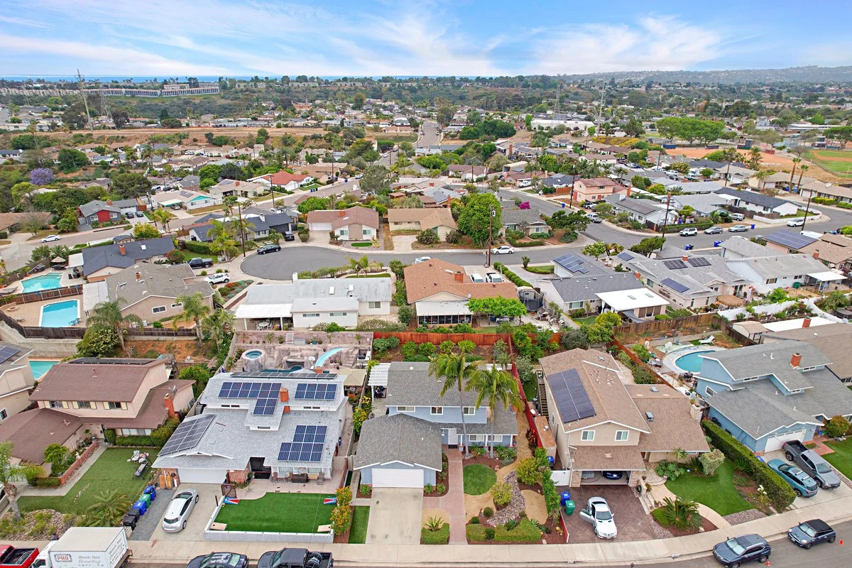 Aerial view of a suburban neighborhood with single-family homes, some with swimming pools, and a landscape with trees and houses.