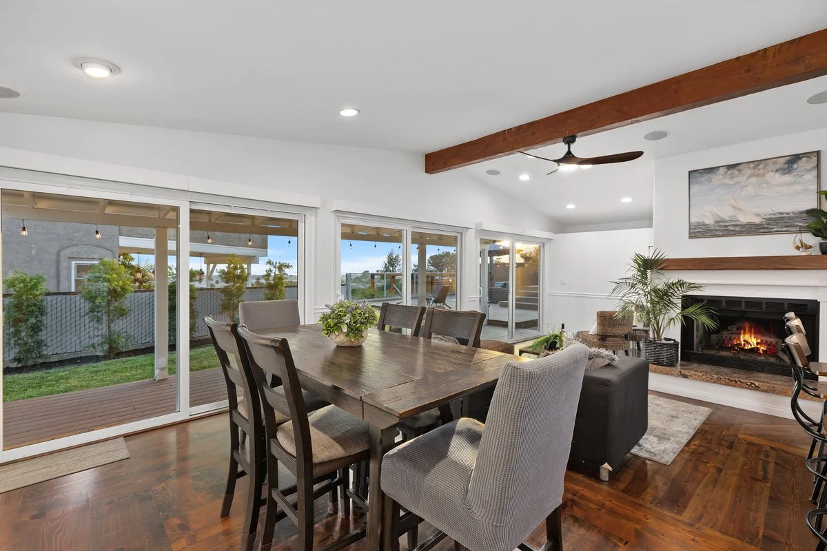 Living room with large sliding glass doors, a wooden dining table with chairs, a fireplace with candles and plants, and a ceiling fan.
