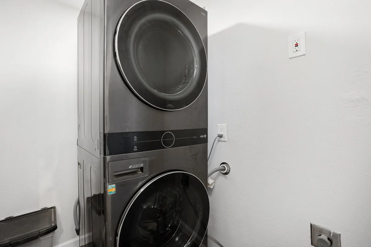 Front-loading stacked washer and dryer in a laundry room, with a white wall and electrical outlets