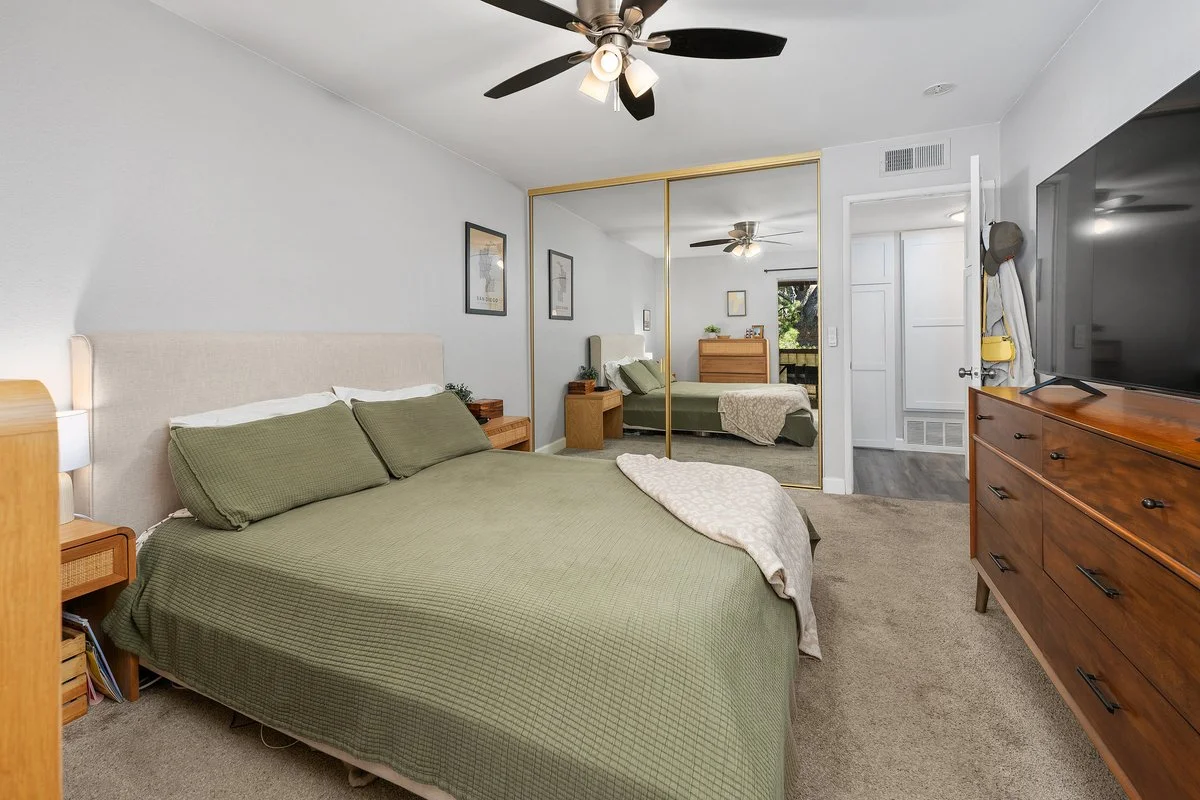 Bedroom with a bed, mirrored closet, wooden dresser, ceiling fan, and door.