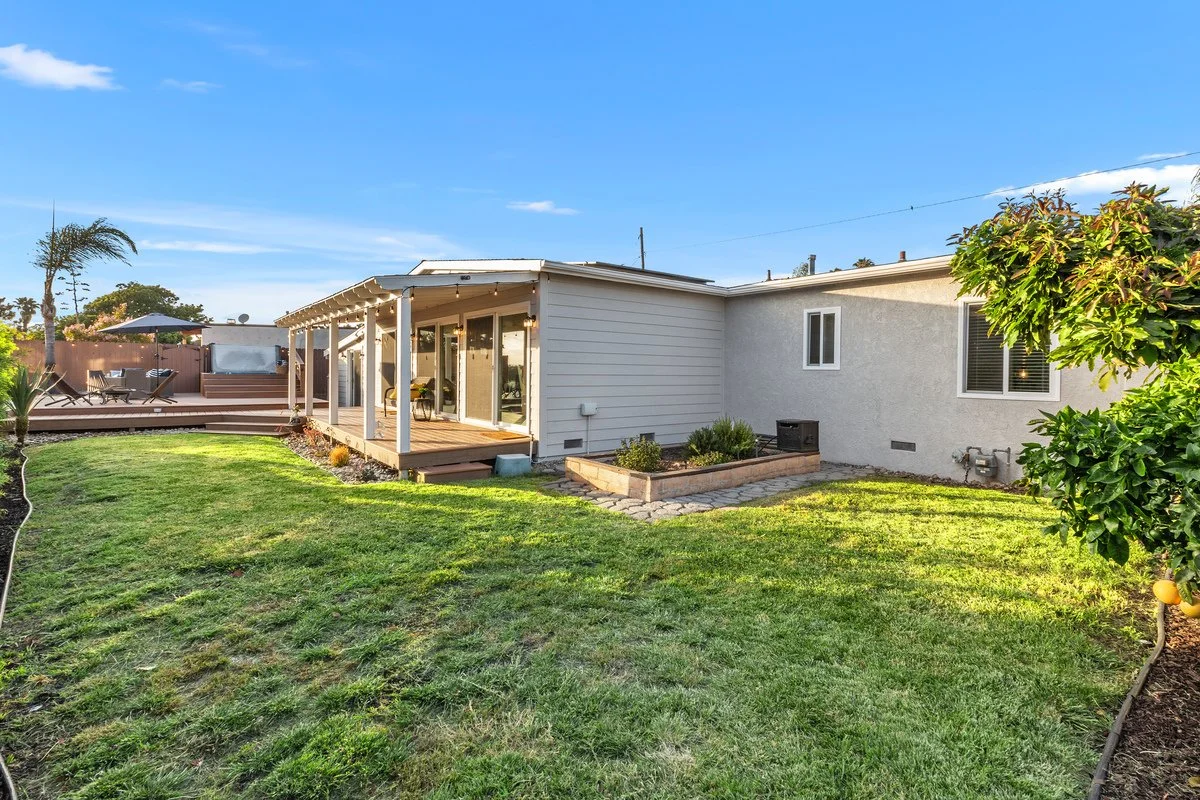 Backyard with a wooden deck, a screened porch, and outdoor seating area, surrounded by greenery and a blue sky.