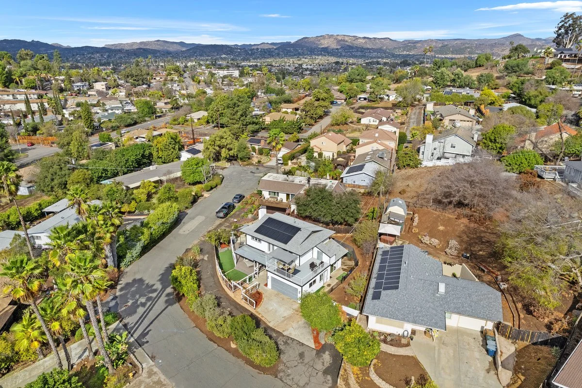 Aerial view of a suburban neighborhood with houses, trees, and streets, with mountains in the background.