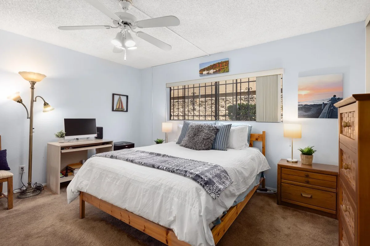 A bedroom with a bed, nightstands, a lamp, end table, dresser, TV, and ceiling fan.