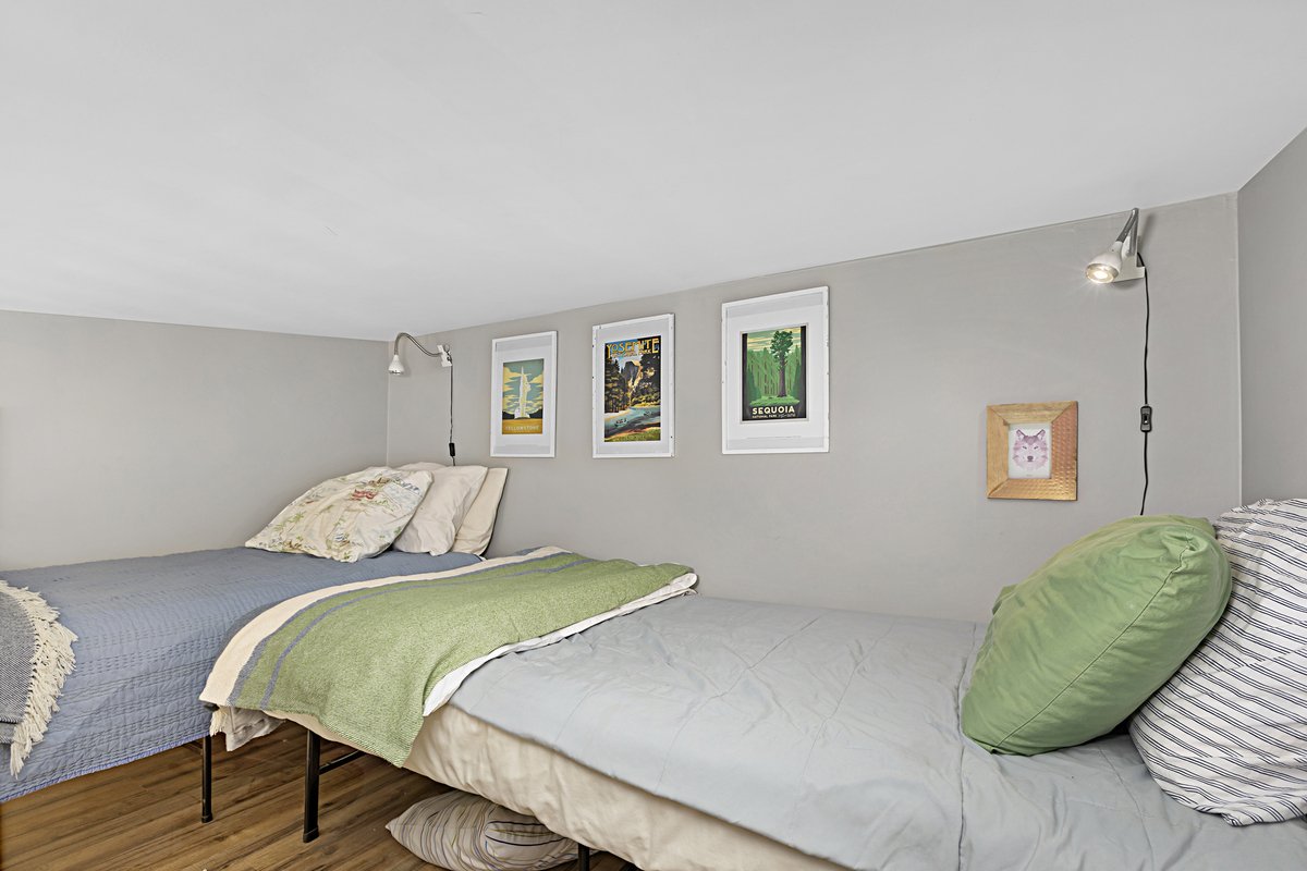 Two beds with pillows and blankets in a small bedroom with framed art on the wall and adjustable reading lamps