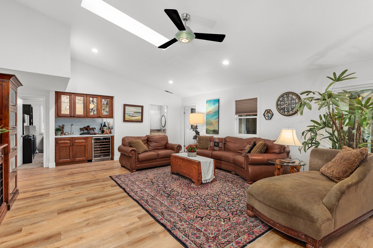 Living room with leather sofas, a wooden chest with a cloth, a patterned rug, a large leafy plant, wall art, and standing lamps.