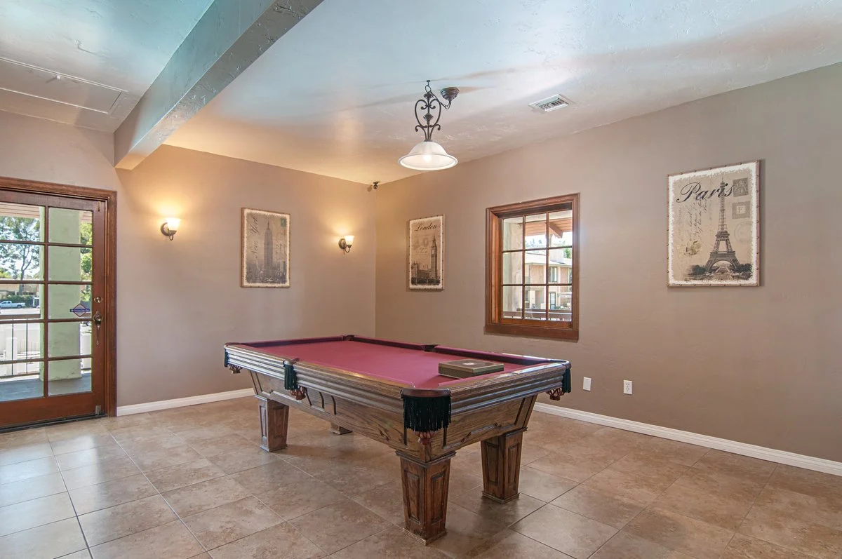 Living room with a pool table, beige walls, two windows, a door, and wall art of Paris landmarks.