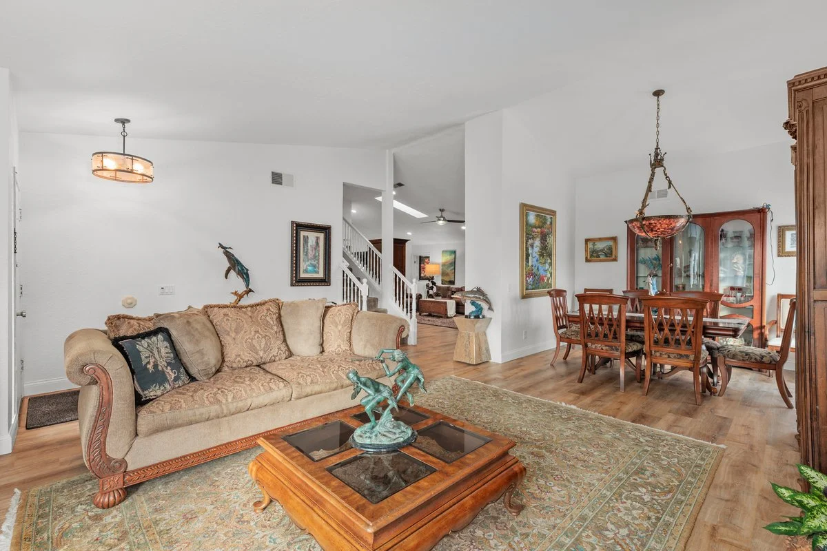 Living and dining room with beige sofa, wooden coffee table, colorful area rug, wooden dining table with chairs, wall art, chandelier, and a china cabinet.