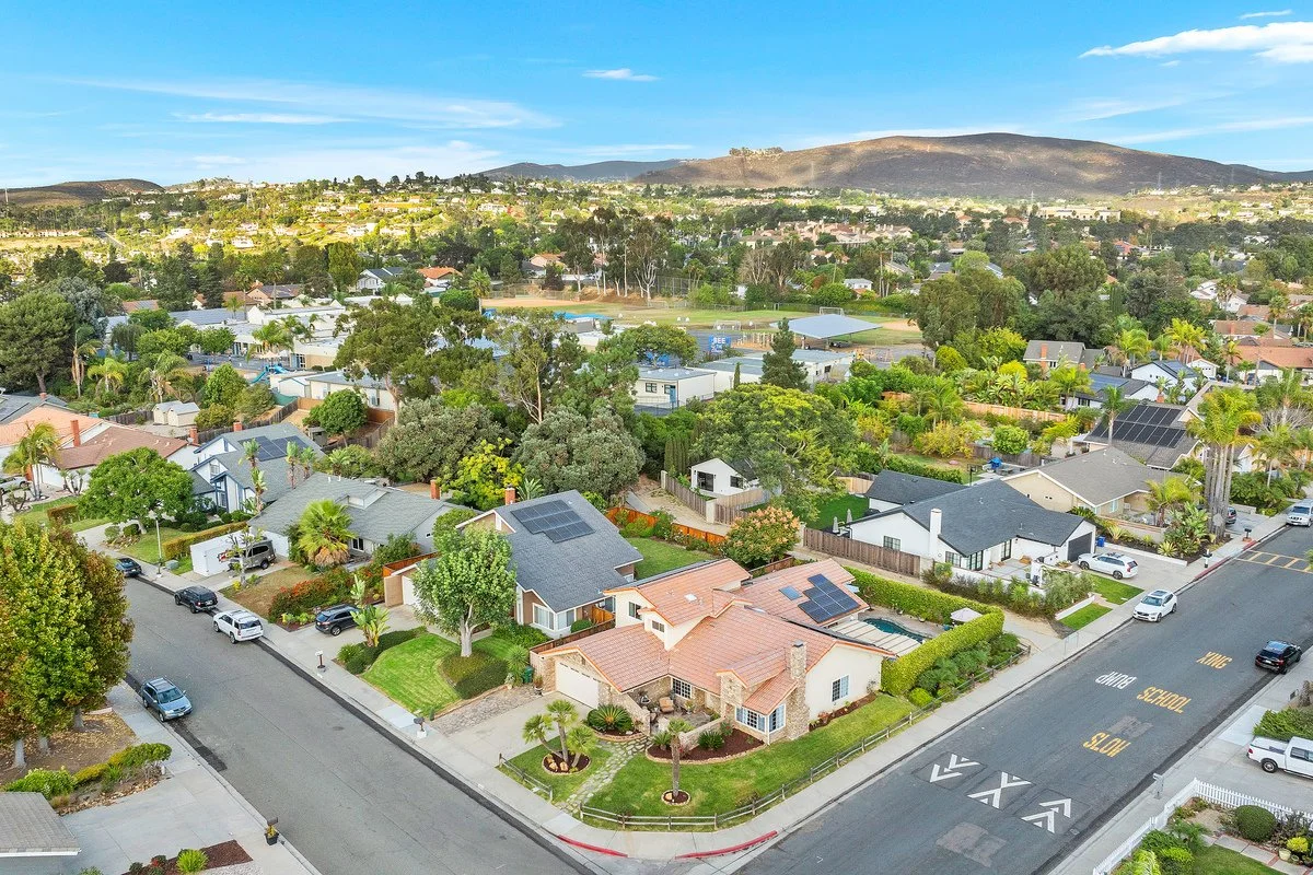 Aerial view of a suburban neighborhood with houses, trees, and streets under a clear blue sky.