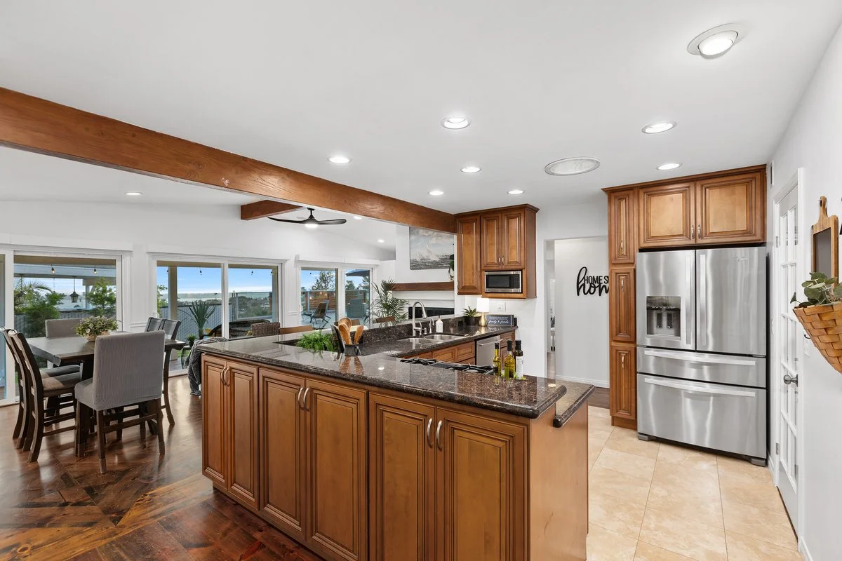 Kitchen with wooden cabinets, stainless steel refrigerator, black granite countertops, and a dining area with a large window view.