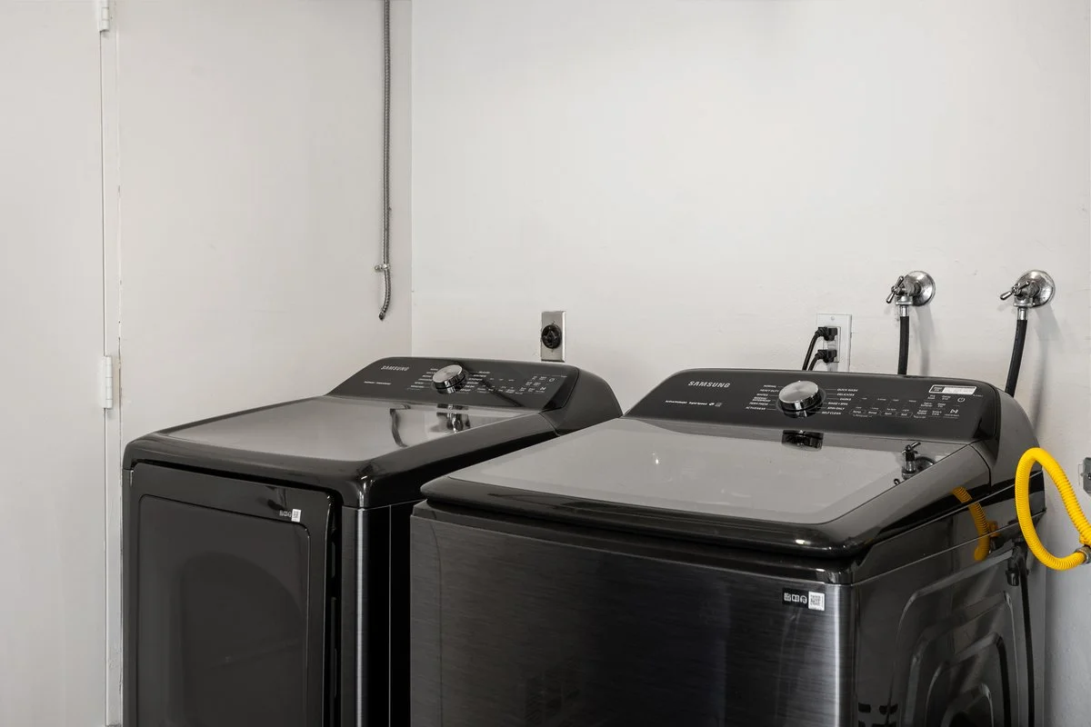 Black top-loading washing machine and dryer in laundry room with white walls.