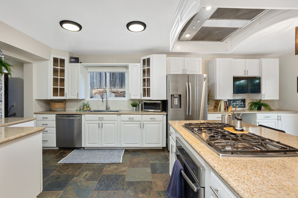 Modern kitchen with white cabinets, stainless steel appliances, granite countertops, and slate tile flooring.