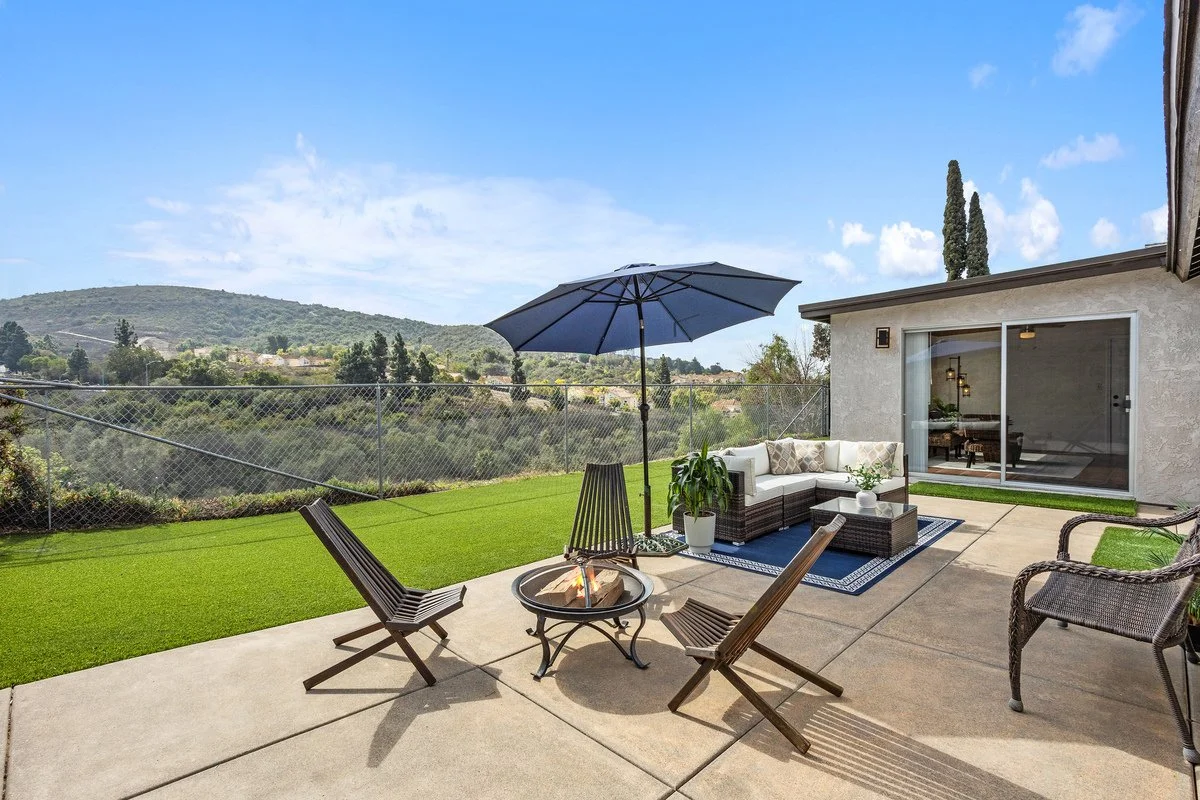 Outdoor patio with a fire pit, lounge chairs, a sectional sofa, an umbrella, and a view of hilly landscape with trees.