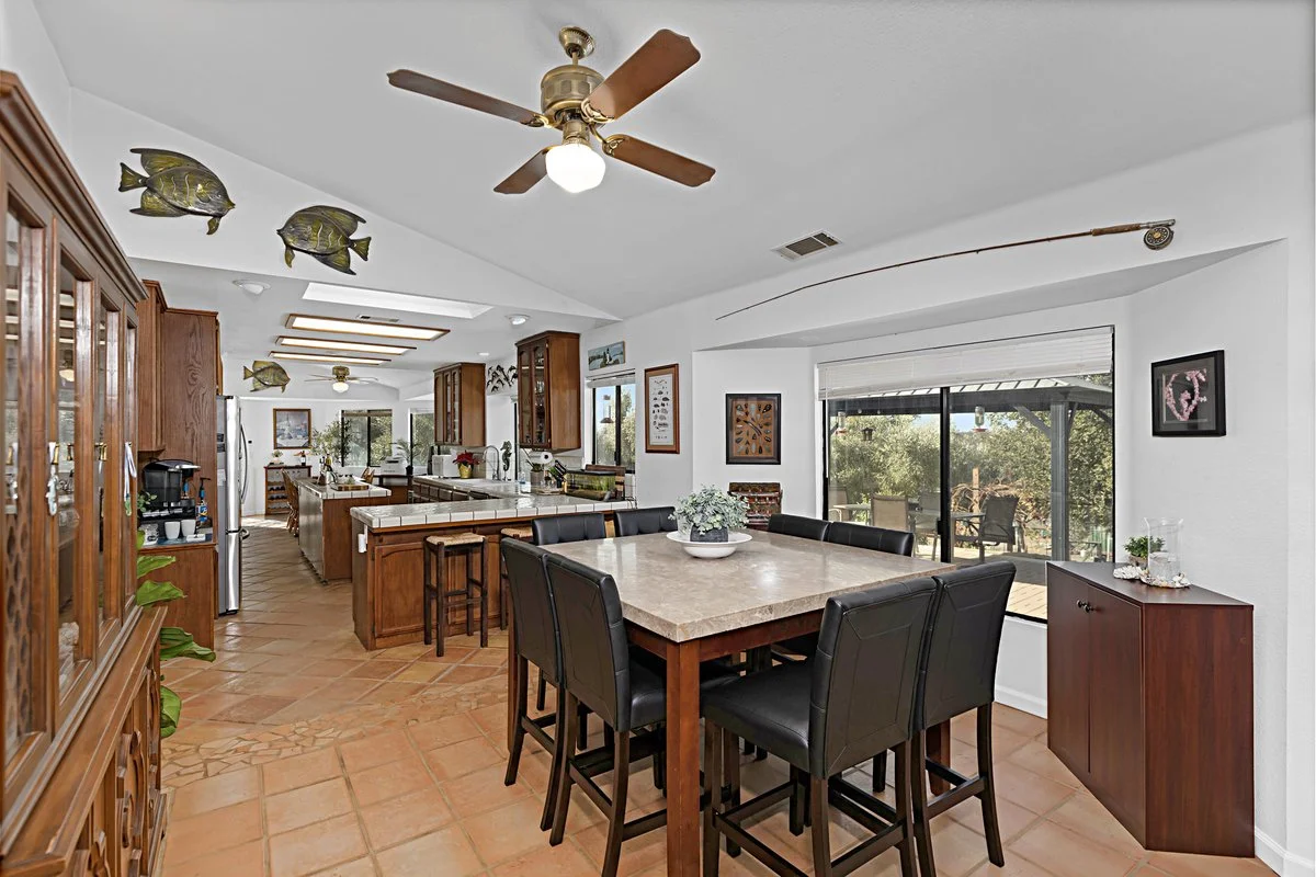 Kitchen and dining area with wooden cabinets, a large central island with bar stools, black dining chairs around a beige table, a sliding glass door leading outside, and decorative fish on the ceiling