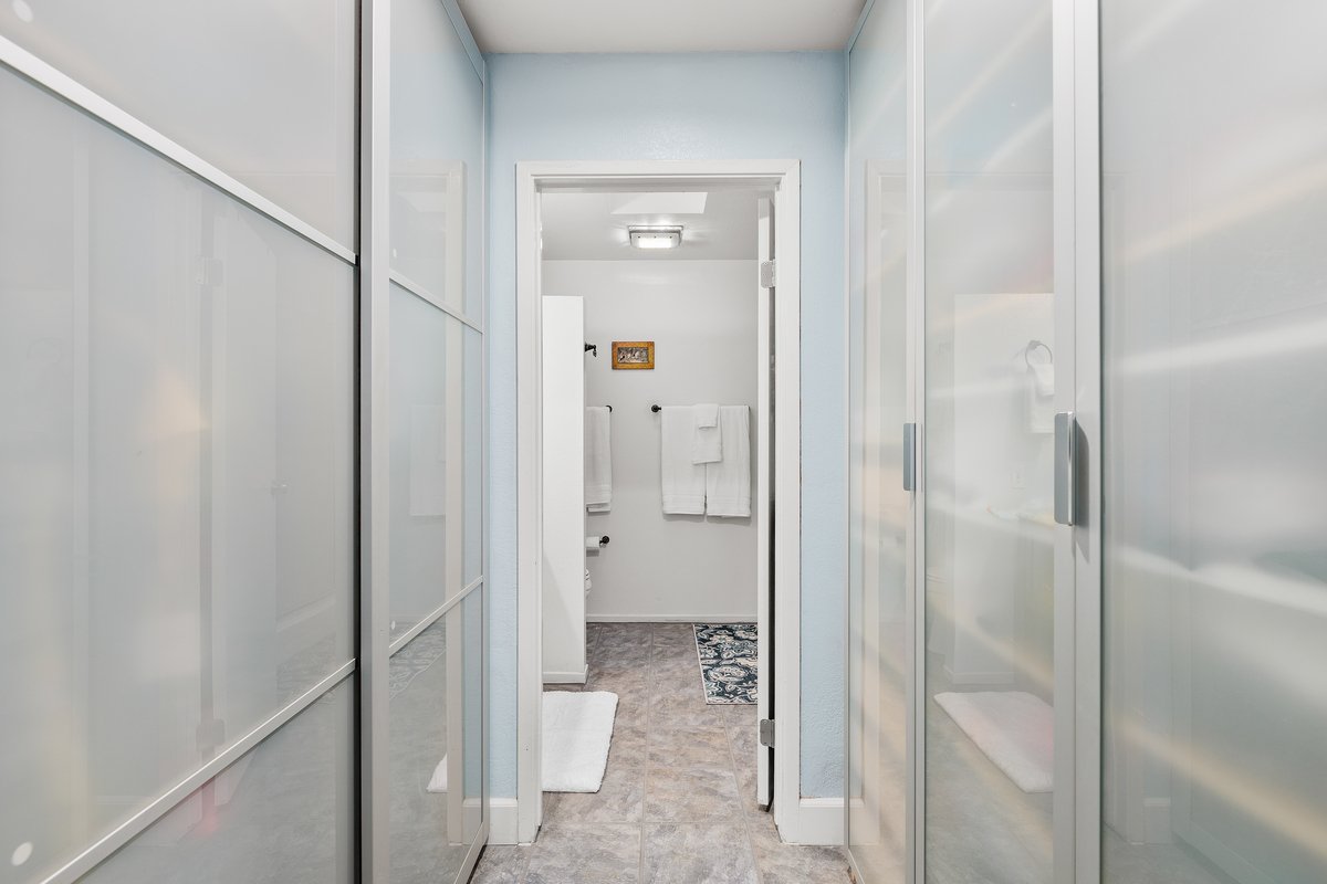 A narrow laundry room with light blue walls and white cabinets on both sides.