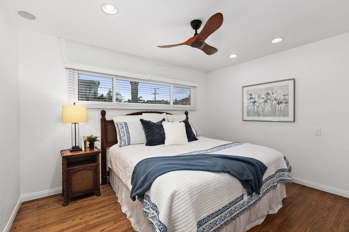 Bedroom with a bed, nightstand with a lamp, artwork on wall, ceiling fan, and window blinds