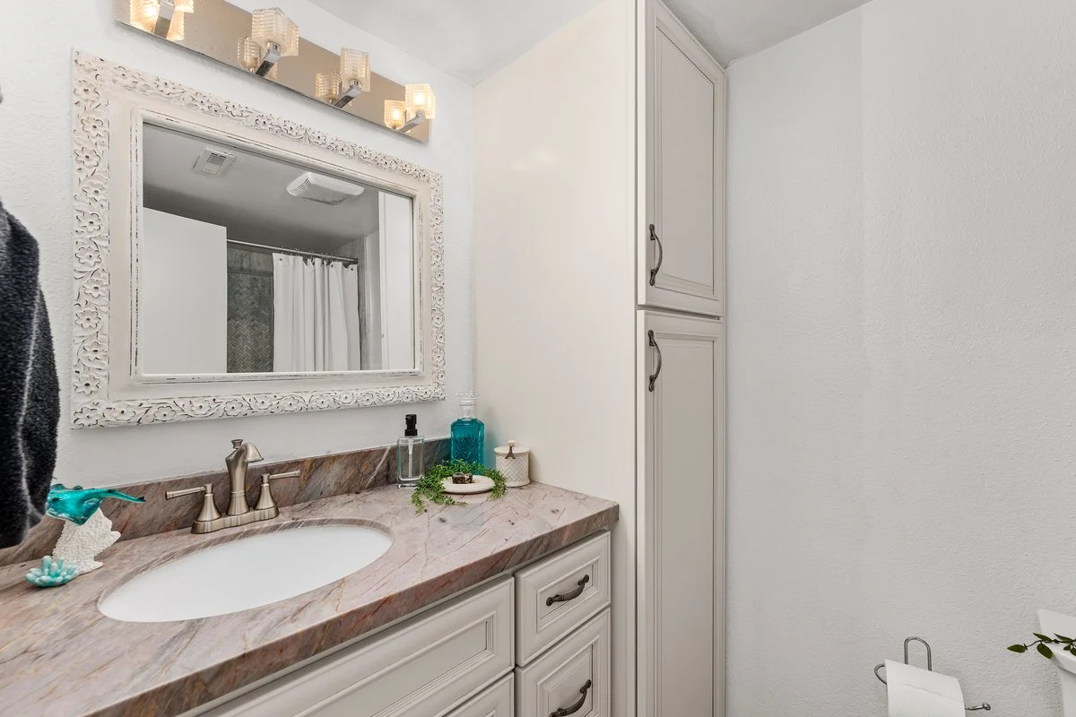 Bathroom vanity with a marble countertop, white cabinet, mirror, and decorative wall light fixtures.