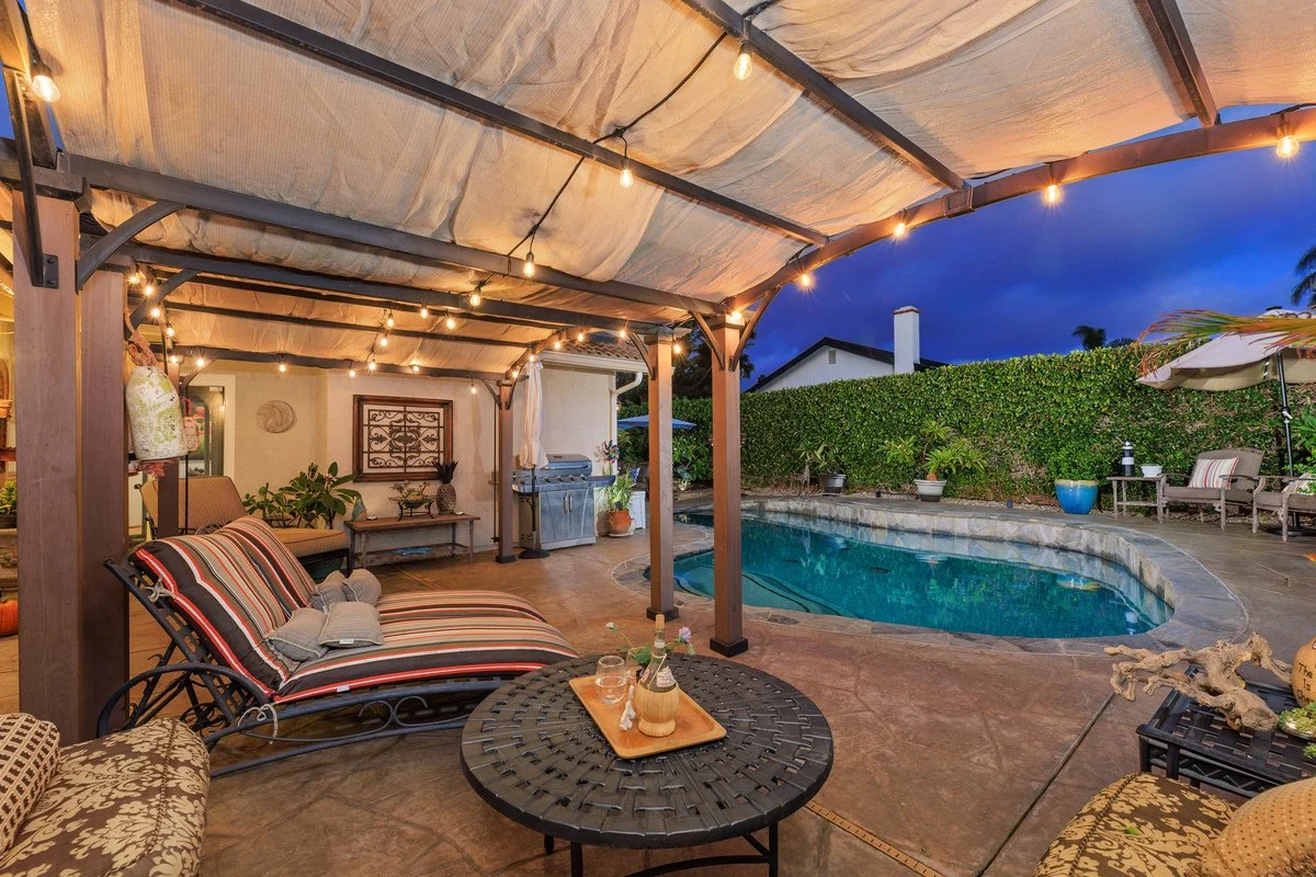 Outdoor backyard patio with string lights, a pool, and patio furniture at dusk.