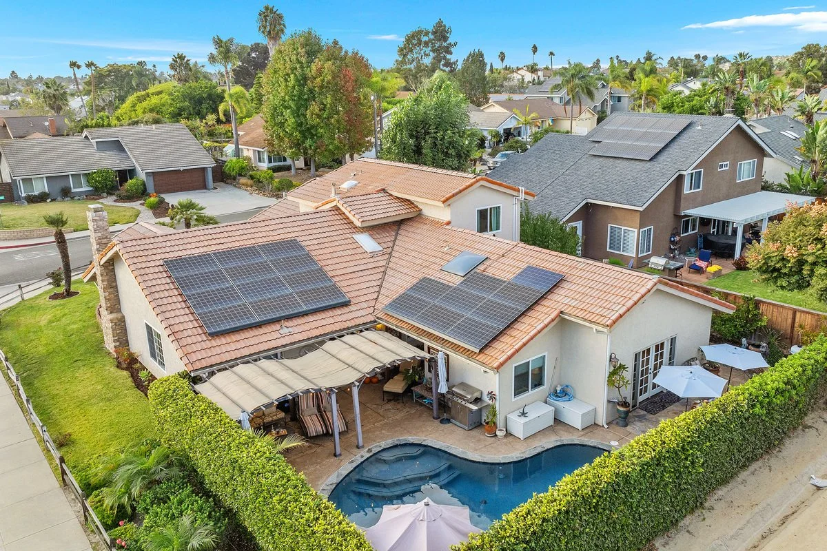 A suburban backyard with a swimming pool, patio furniture, and solar panels on the roof of the house.
