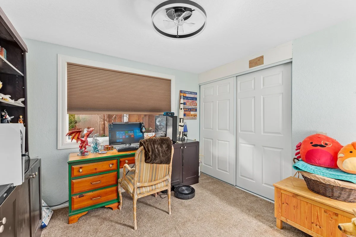 A cozy home office corner with a window, desk, computer, and various decorations including plush toys and a wooden storage bench.