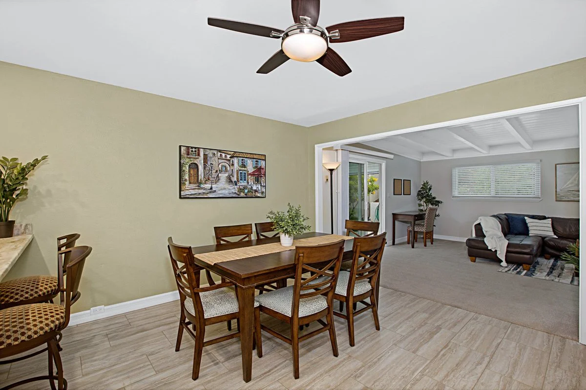 Open-concept dining and living room with ceiling fan, dining table with six chairs, and sofa with pillows and throw blanket.