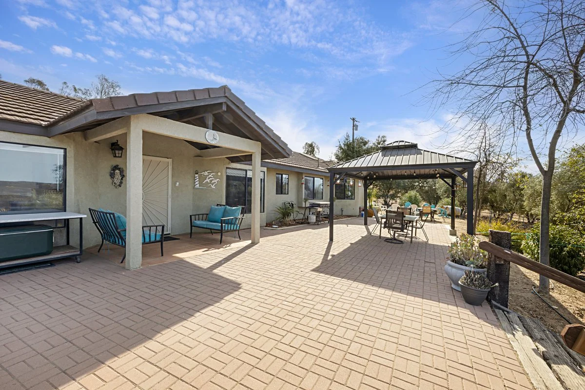 Spacious backyard patio with seating area, gazebo, potted plants, and view of trees and sky